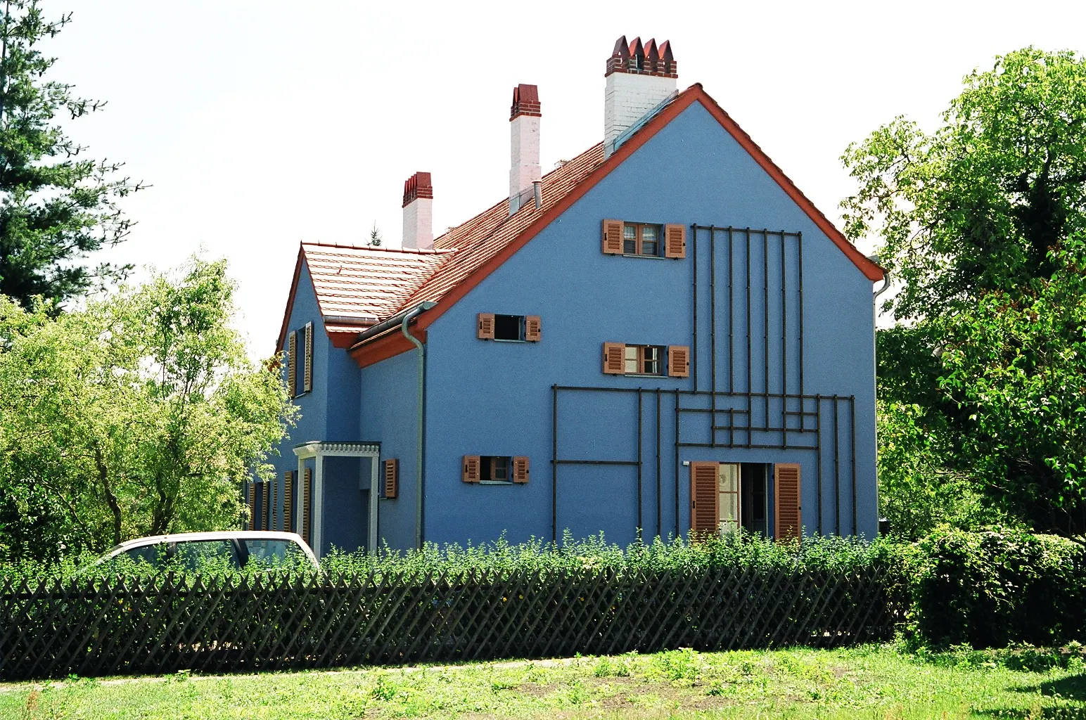 Blaues Haus der Tuschkastensiedlung mit Spalier an der Fassade und grünem Garten.